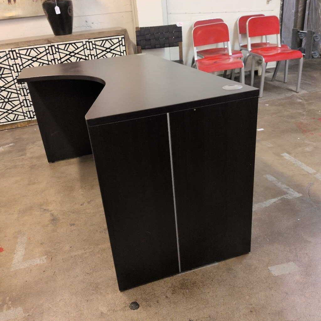 Black L-shaped reception desk in an indoor setting with red chairs and patterned wall.