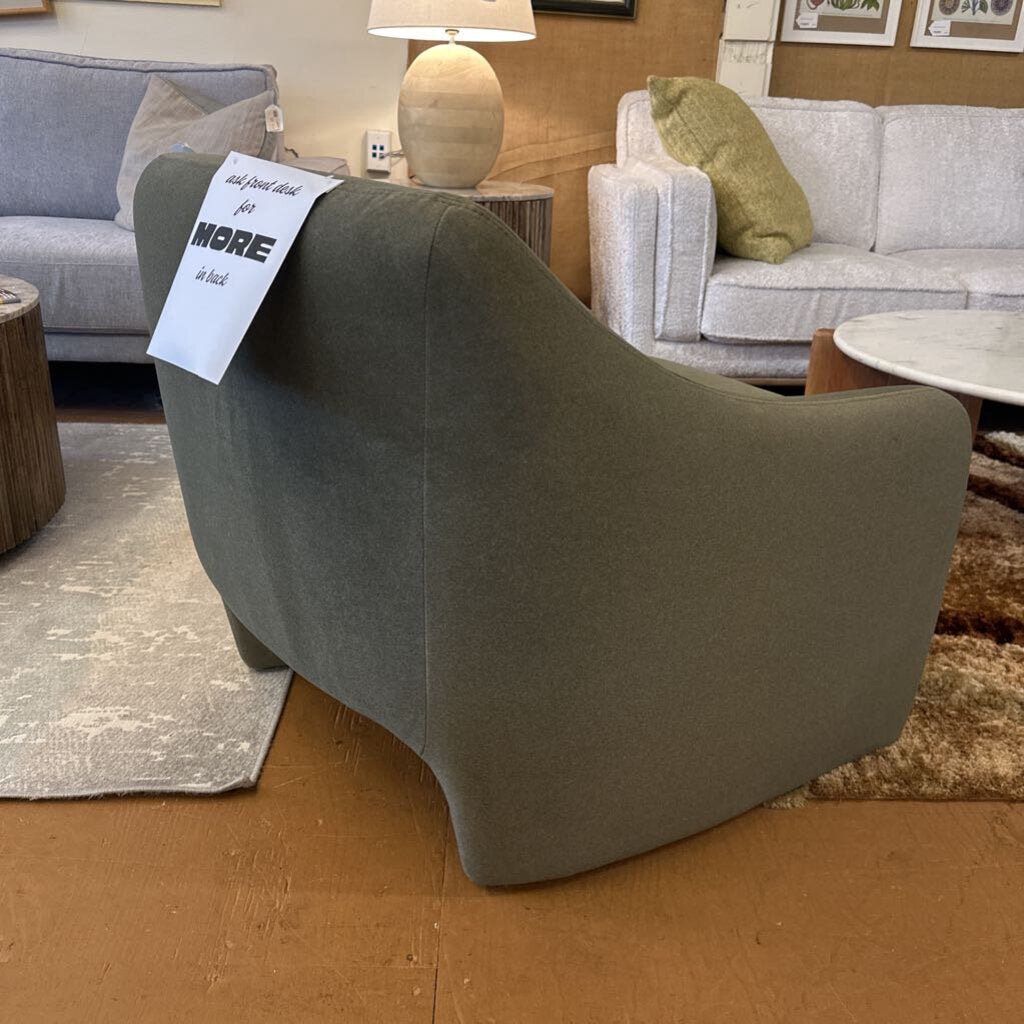 Gray armchair in a showroom with a price tag, surrounded by other furniture.