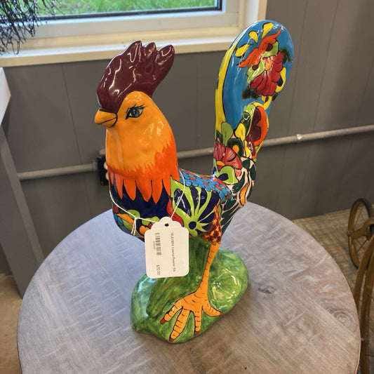 Colorful ceramic rooster sculpture on a round table with a window in the background.