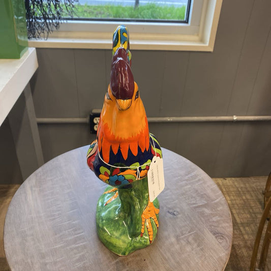 Colorful ceramic rooster sculpture on a round table with a window in the background.