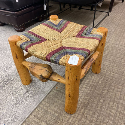 Wooden stool with a colorful woven seat on a carpeted floor.