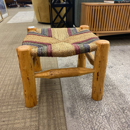 Wooden stool with a multicolored woven seat in a room setting.