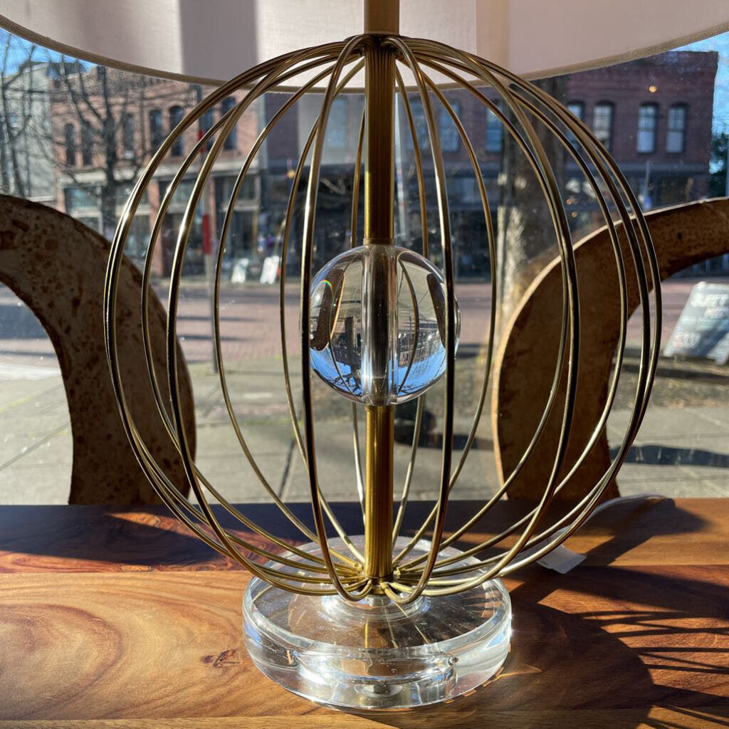 Decorative lamp with gold metal cage and clear glass base on a wooden surface.