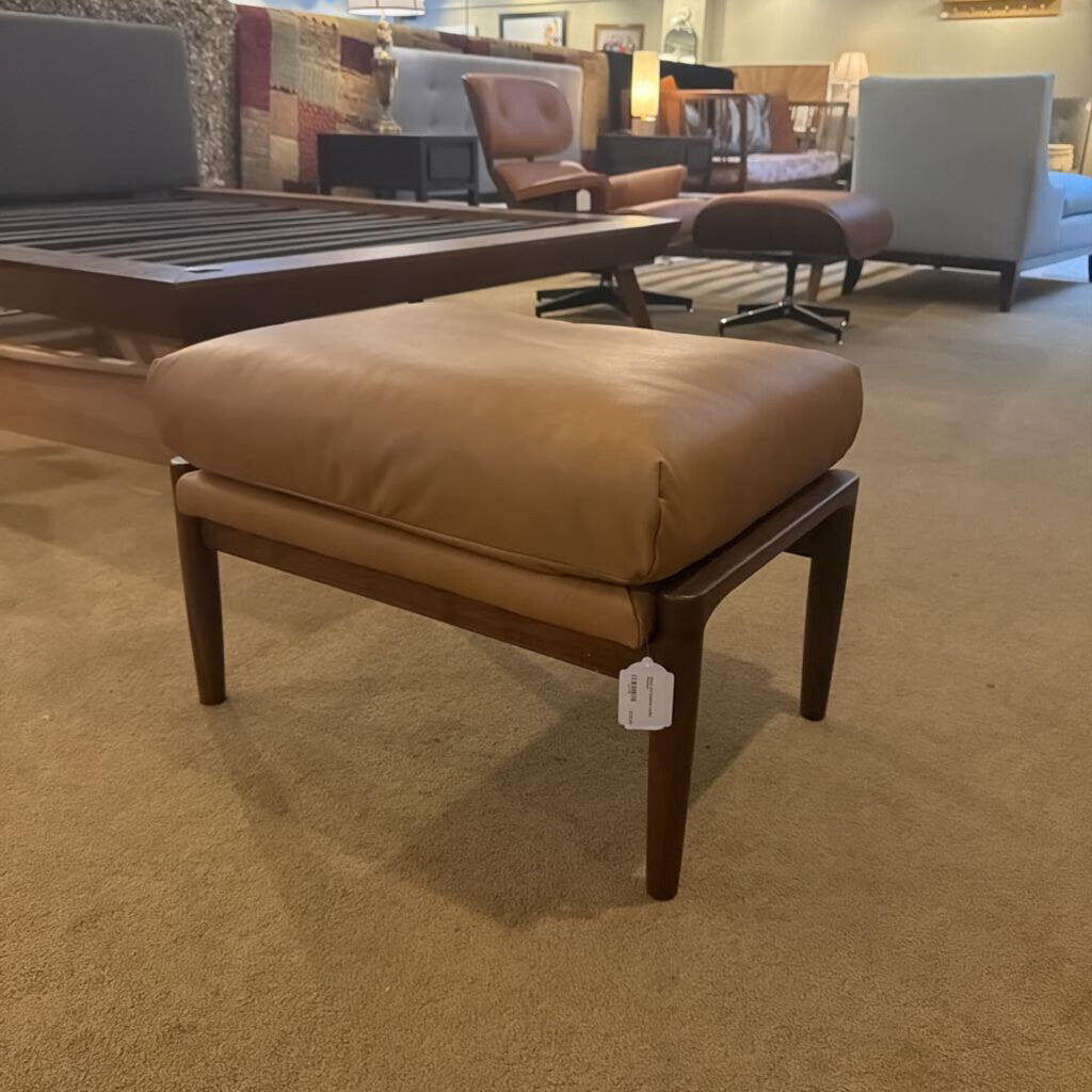Brown leather ottoman with wooden legs in a showroom setting