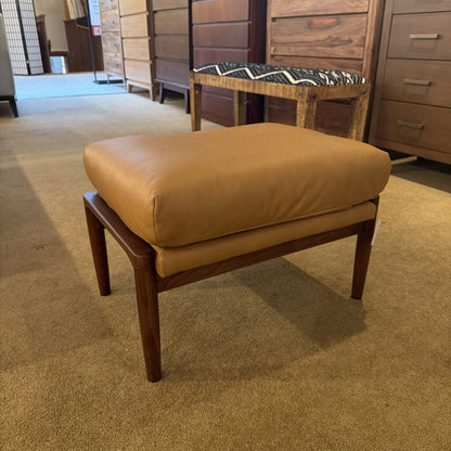 Brown ottoman with wooden legs in a room with furniture