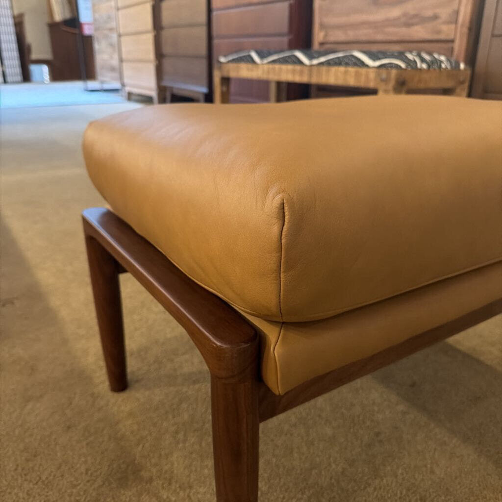 Brown leather ottoman with wooden legs on a carpeted floor.