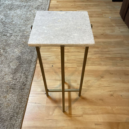 Small square table with marble top and gold legs on a wooden floor
