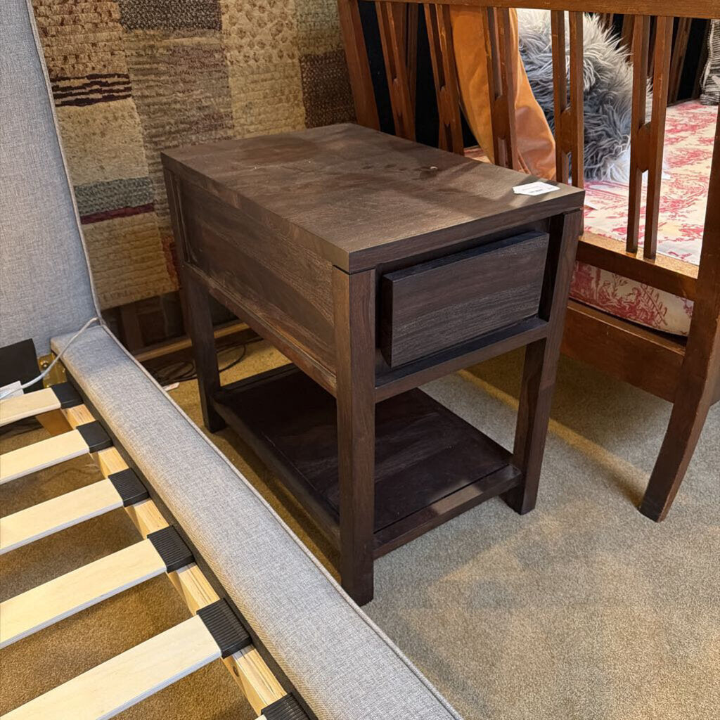 Wooden nightstand next to a bed with a textured wall in the background