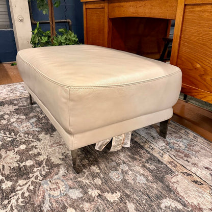 Beige ottoman on a patterned rug with a wooden cabinet in the background