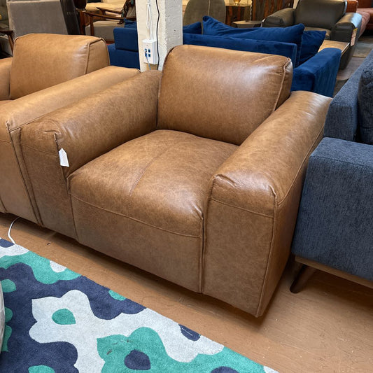 Brown leather sofa in a showroom with blue and gray sofas in the background.