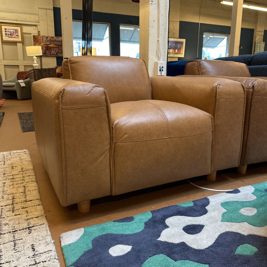 Brown leather sofa in a showroom with floral rug and mirrors on the wall.