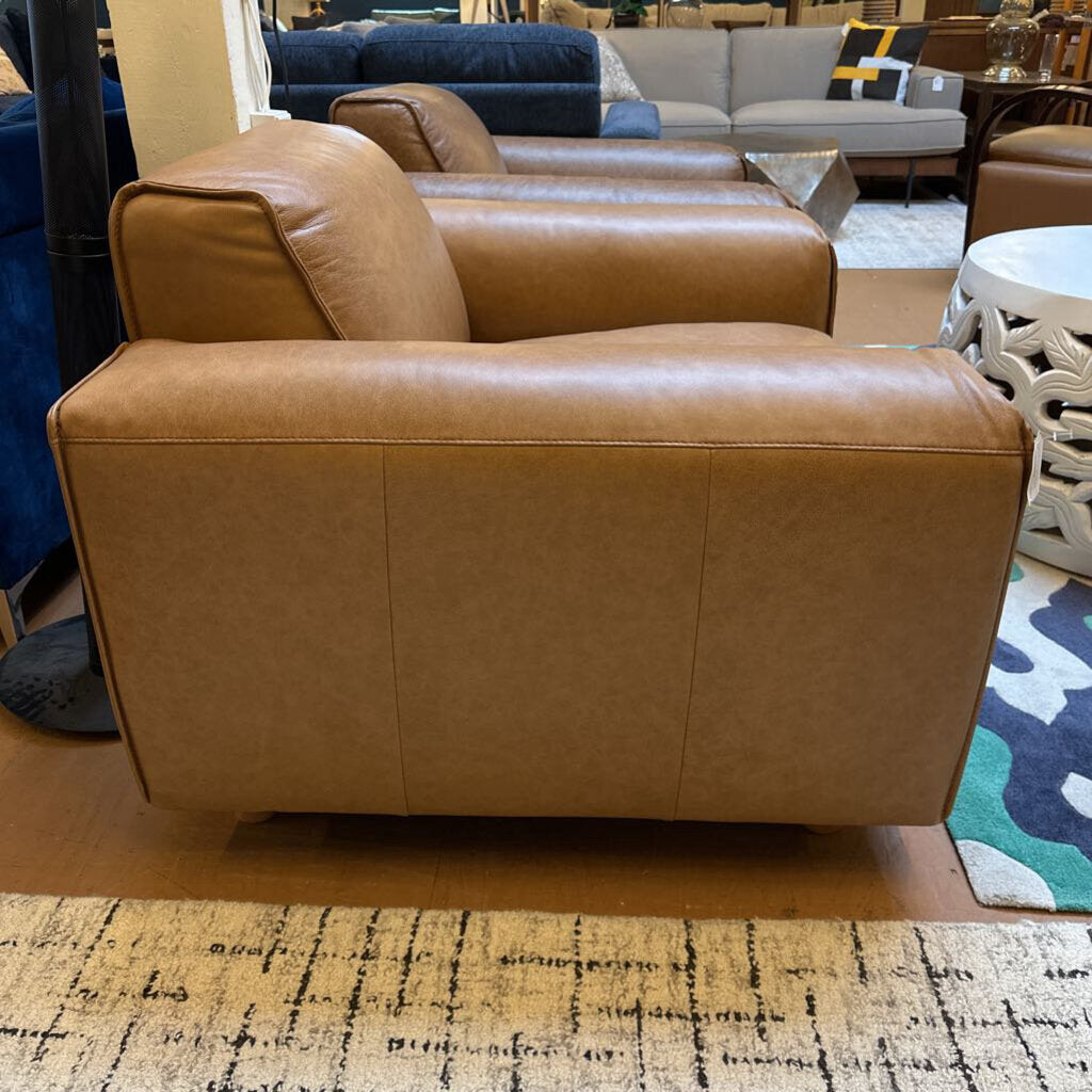 Brown leather armchair in a showroom setting with other furniture.