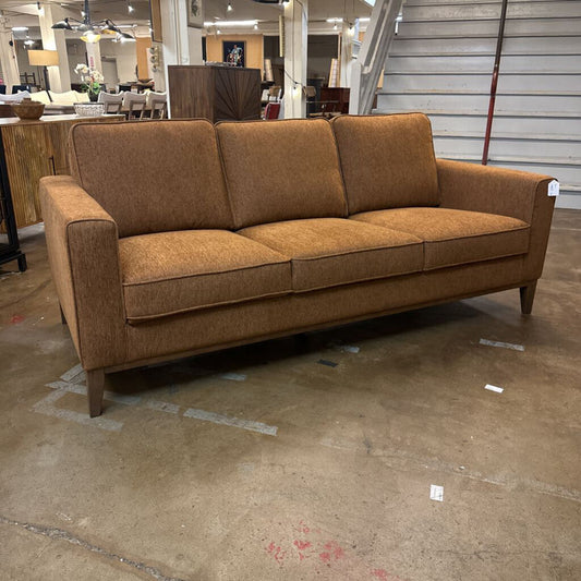 Brown sofa in a showroom setting with mirrors and furniture in the background.