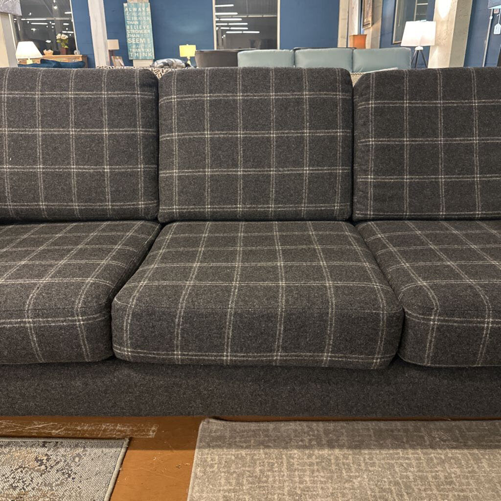 Gray plaid sectional sofa in a store setting with lamps and decor in the background.