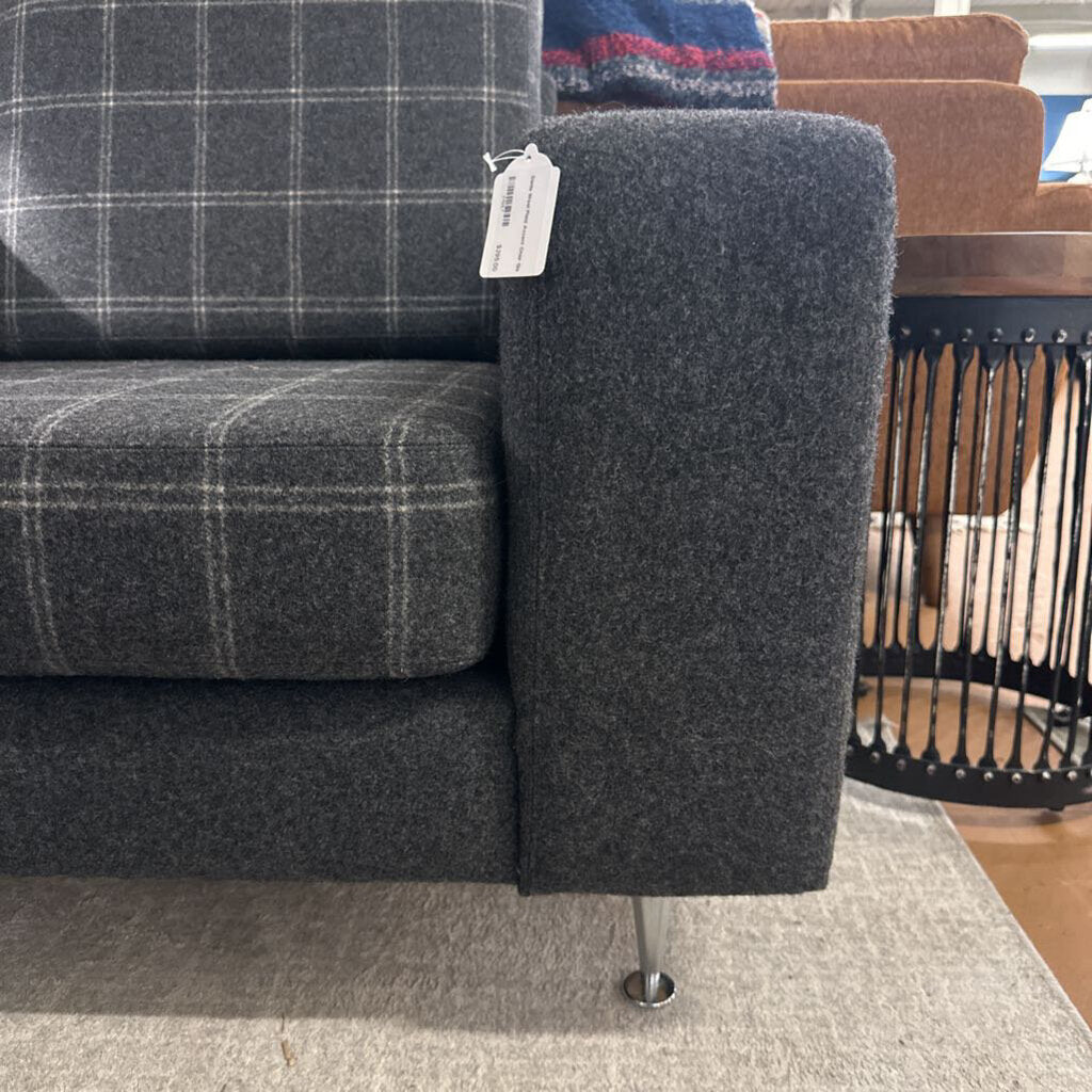 Gray plaid sofa with a tag, wooden chair in the background