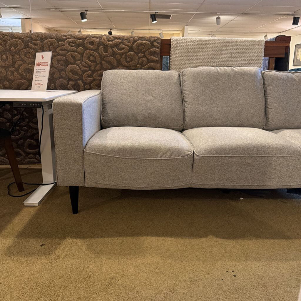Gray sofa in a store setting with carpeted floor and patterned walls.