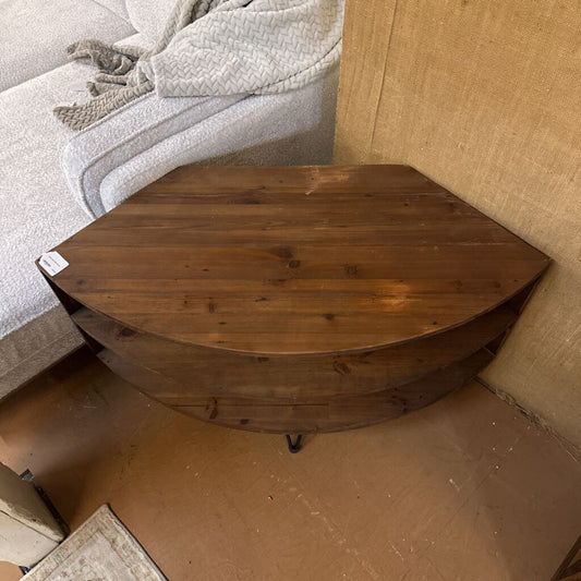 Wooden corner table in a room setting with furniture and carpet.