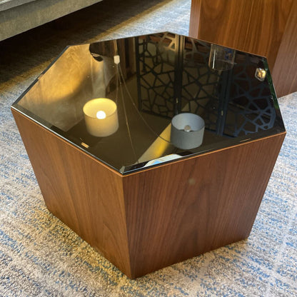 Hexagonal wooden side table with a glass top, candle, and small bowl on a carpeted floor.
