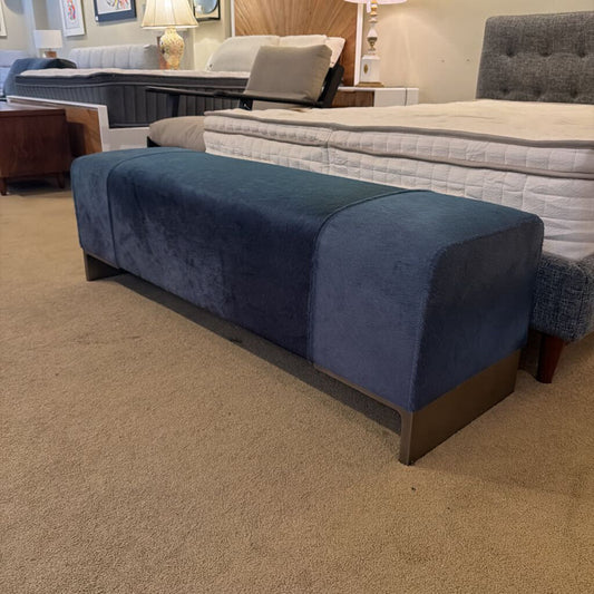 Blue upholstered bench in a showroom setting with beds in the background