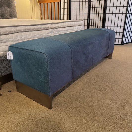 Blue upholstered bench on a carpeted floor with a mattress in the background
