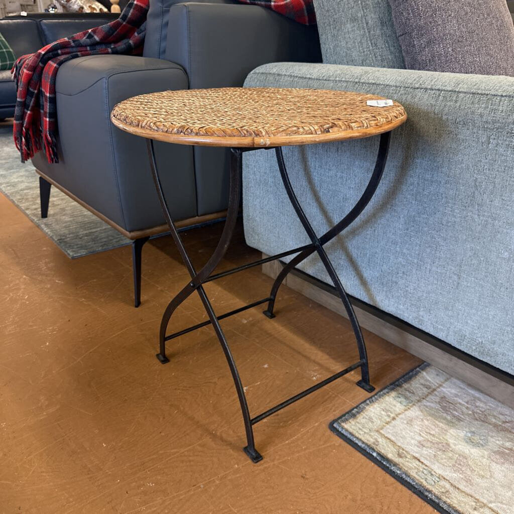 Small wicker table with black metal legs in front of a gray sofa.