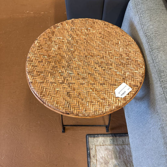 Round woven table with a price tag on a wooden floor next to a gray sofa.