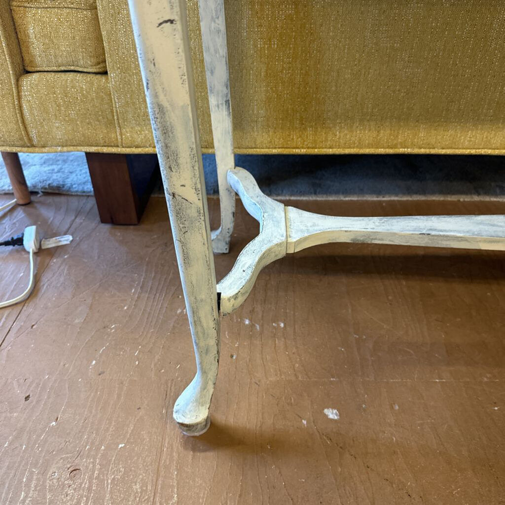 Close-up of a wooden chair leg on a wooden floor with a yellow upholstered chair in the background.