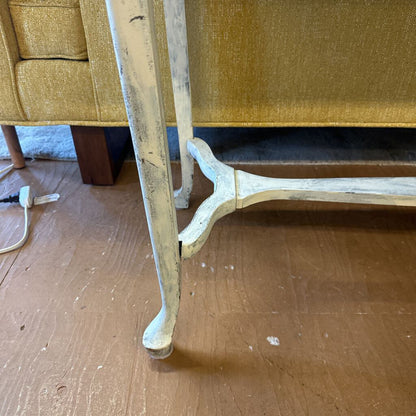 Close-up of a wooden chair leg on a wooden floor with a yellow upholstered chair in the background.