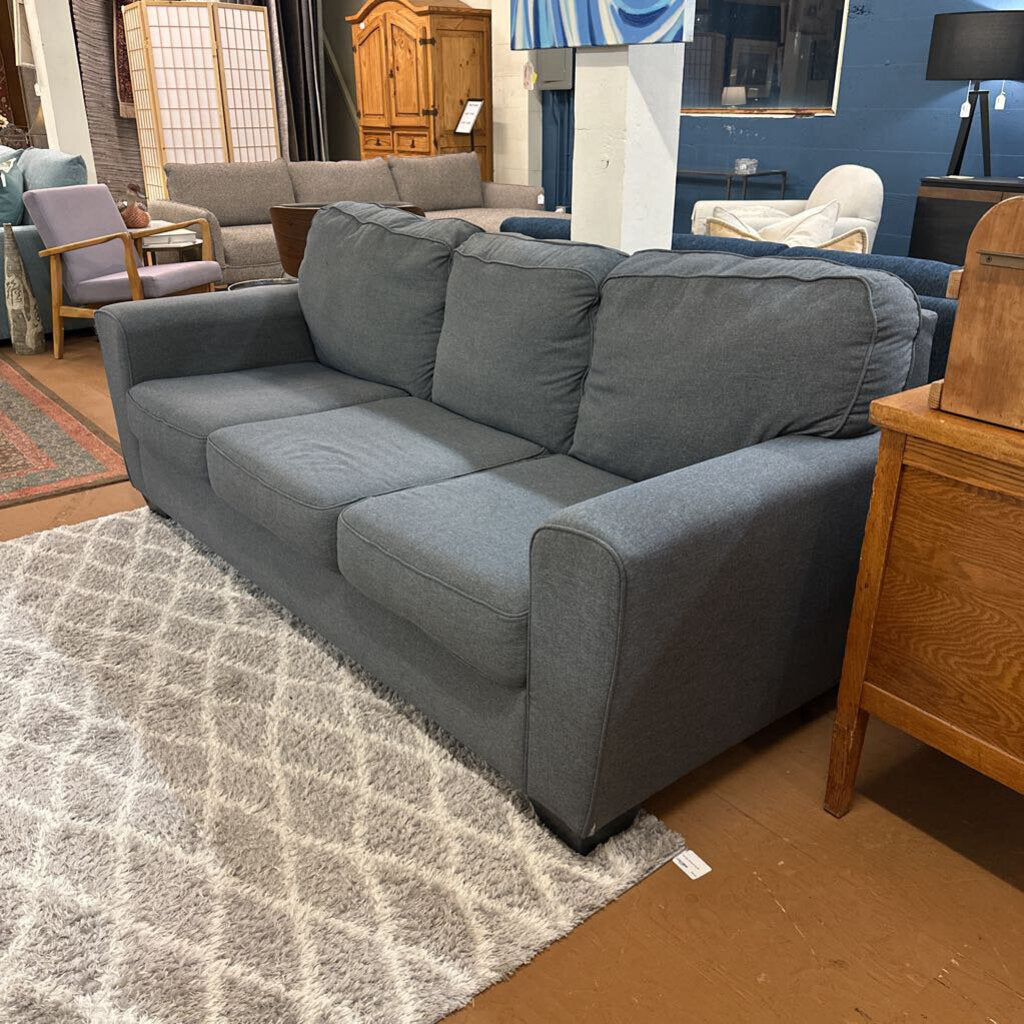 Gray sofa in a living room setting with furniture and decor around it.