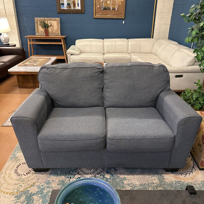 Gray sofa in a living room setting with a blue wall and furniture.
