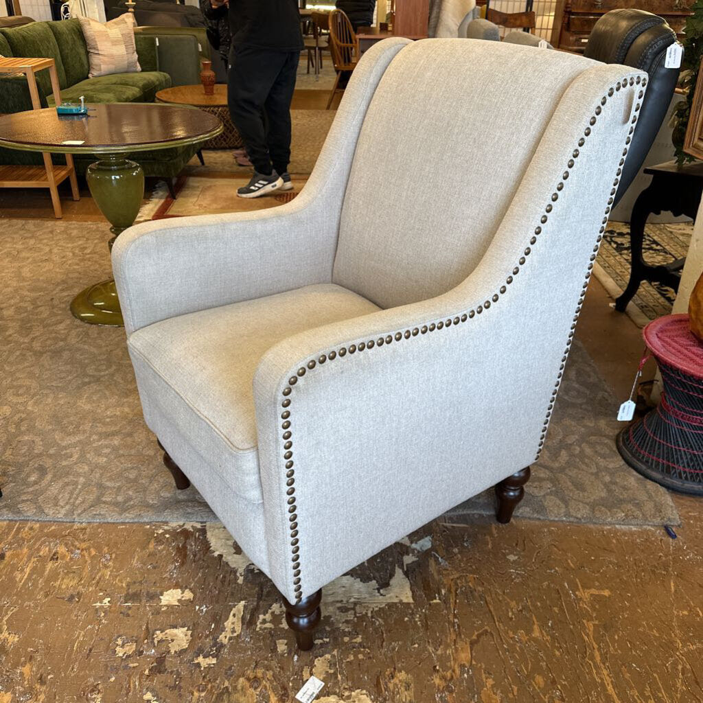 Beige armchair with nailhead trim in a furniture store setting