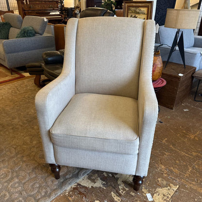Beige armchair in a furniture store setting with other chairs and decor items.