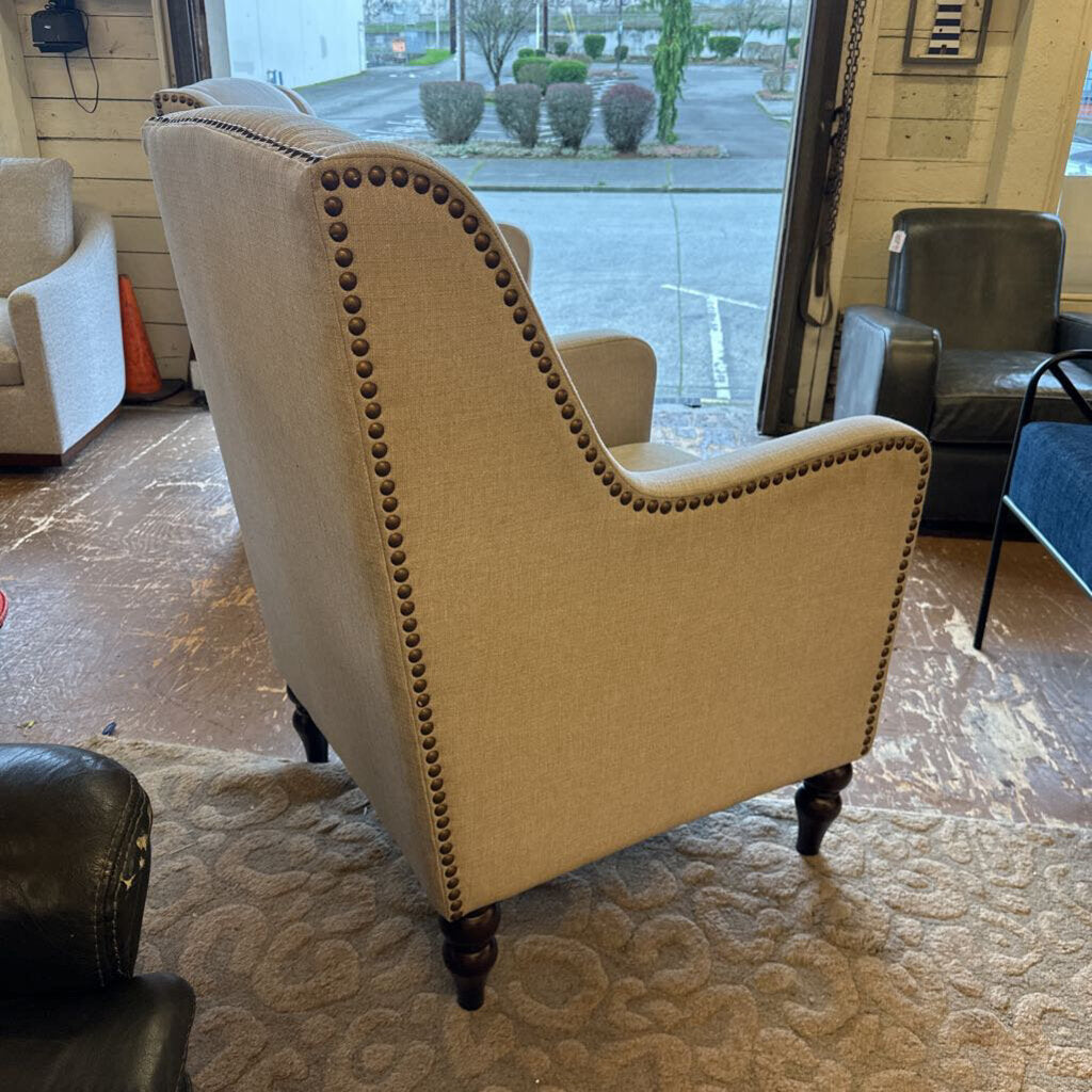 Beige armchair with nailhead trim in a room with other furniture and a glass door.