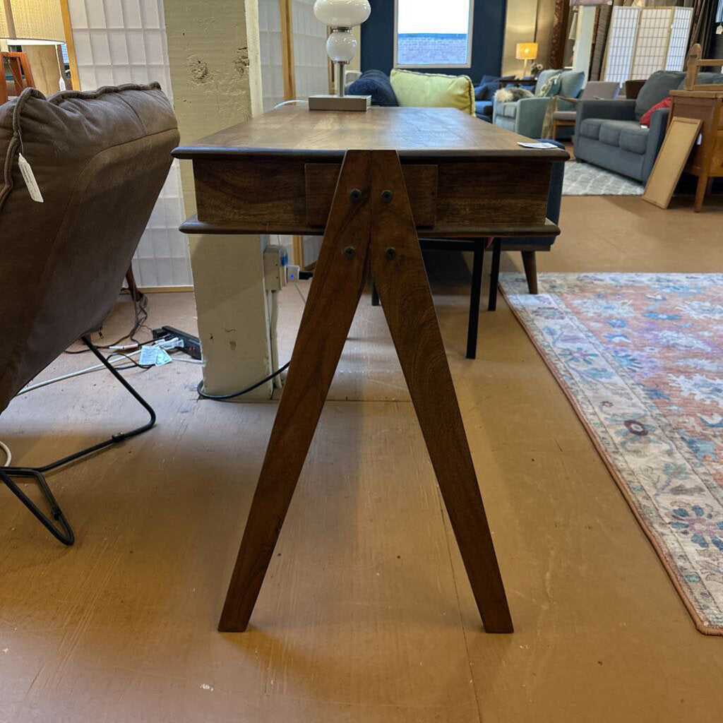 A slim, dark wood writing desk with a minimalist rectangular top, two open storage cubbies, and angled A-frame legs, shown on a neutral carpet.