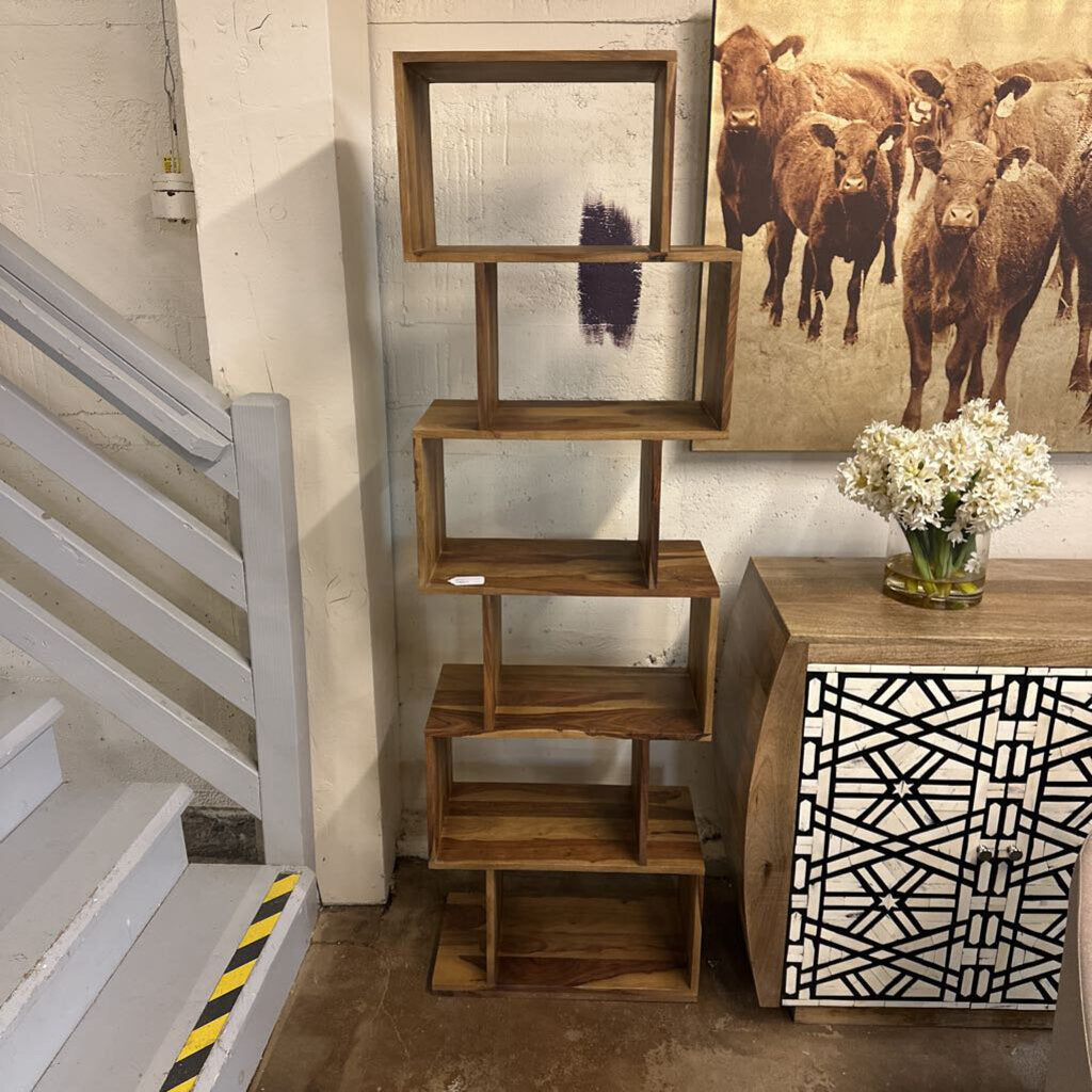 Wooden bookshelf next to a staircase with decorative elements and a cow painting on the wall.