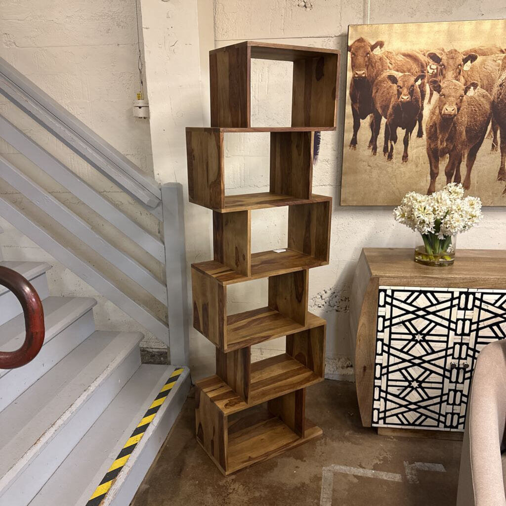 Wooden bookshelf next to a staircase with a decorative painting of cows on the wall.
