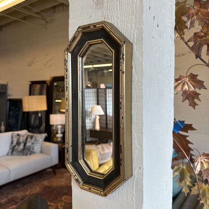 Decorative wall mirror with black and gold frame on a white wall