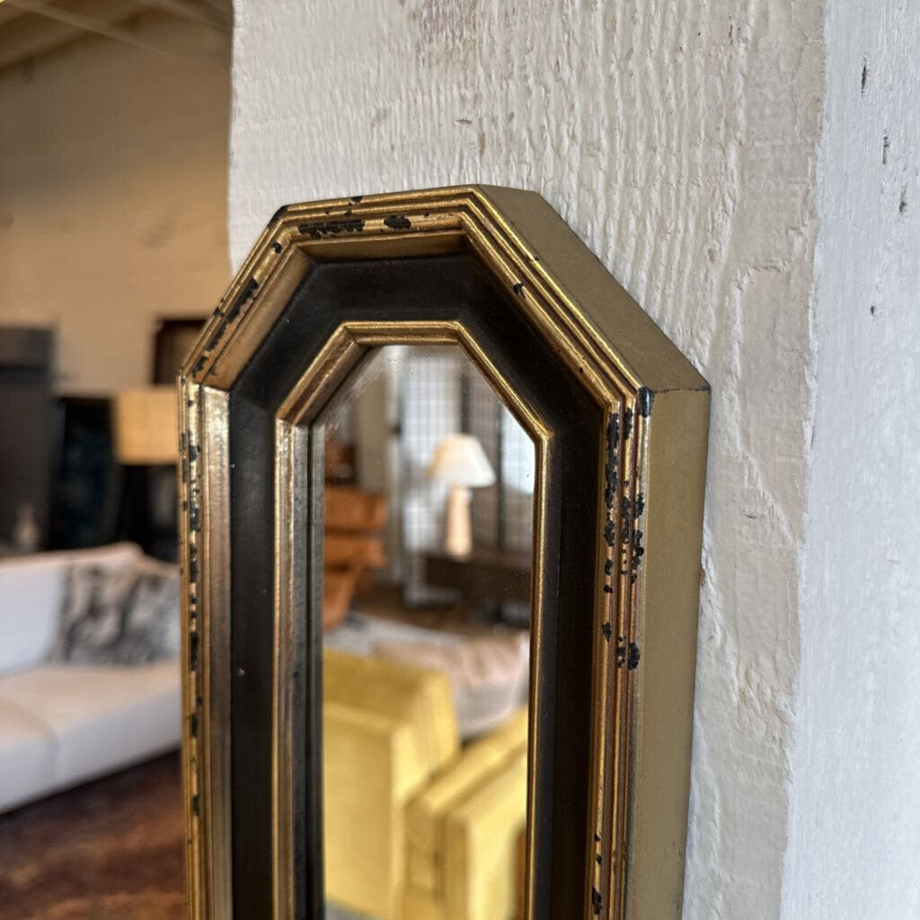 Decorative wall mirror with gold frame leaning against a textured white wall.