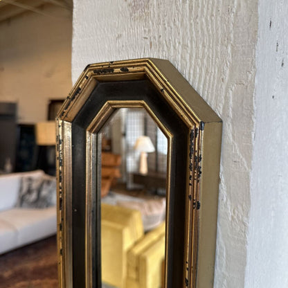 Decorative wall mirror with gold frame leaning against a textured white wall.
