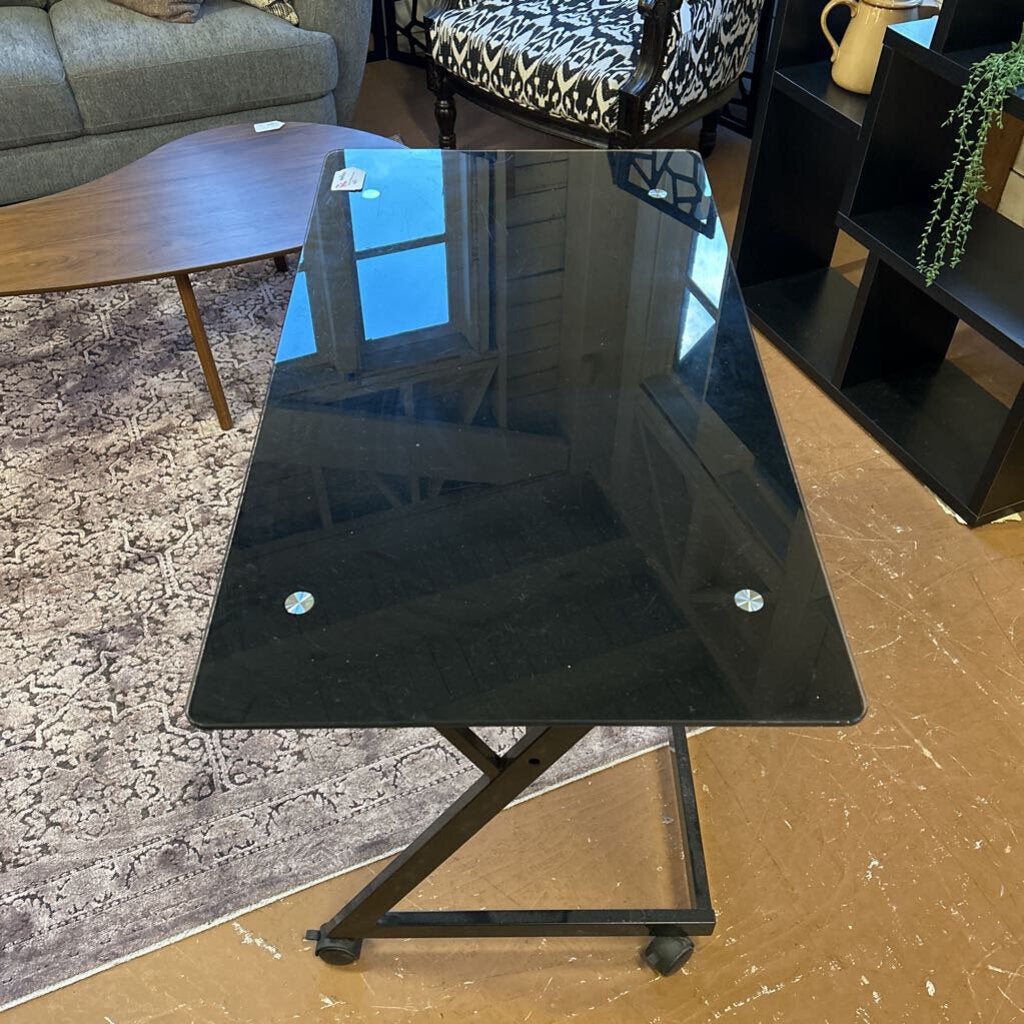 Black glass table in a living room setting with a sofa and coffee table in the background.