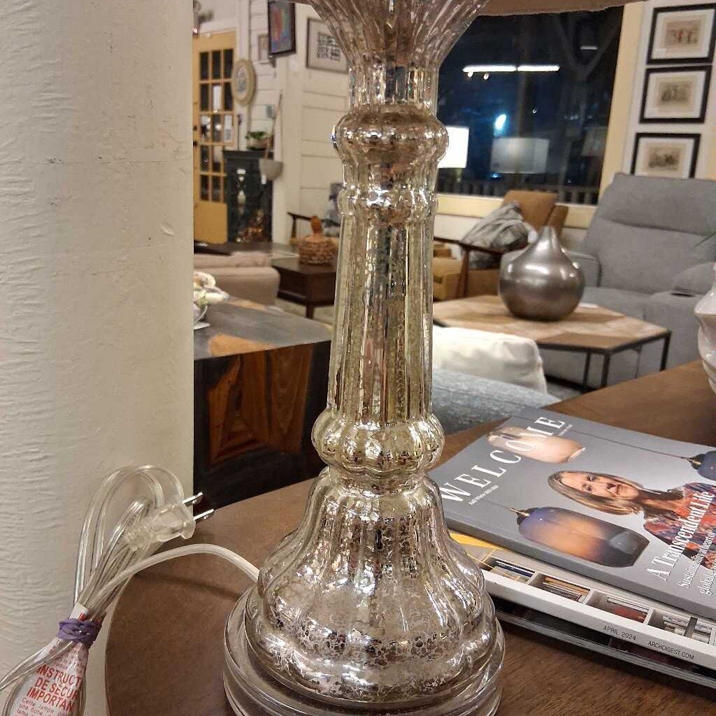 Mercury glass table lamp on a wooden surface with a magazine in the background