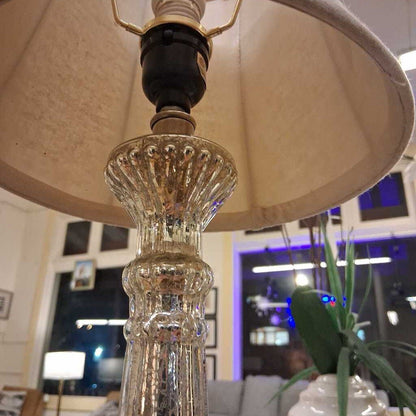 Close-up of a lamp with a decorative glass bulb and beige lampshade in an indoor setting.
