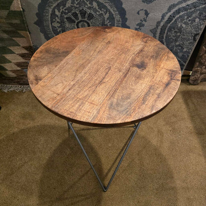 Round wooden side table with metal legs on a carpeted floor.