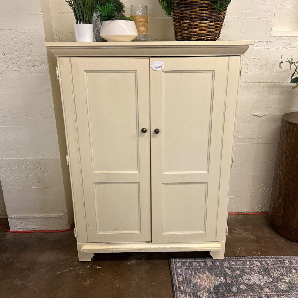 Beige cabinet with two doors against a white brick wall.