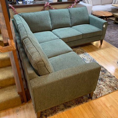 Green sectional sofa in a living room setting with wooden floor and staircase.