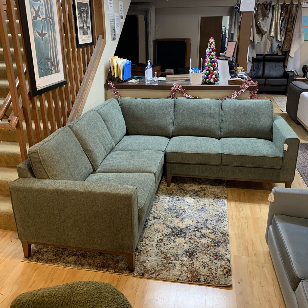 Green sectional sofa in a living room setting with a staircase and decorative items.