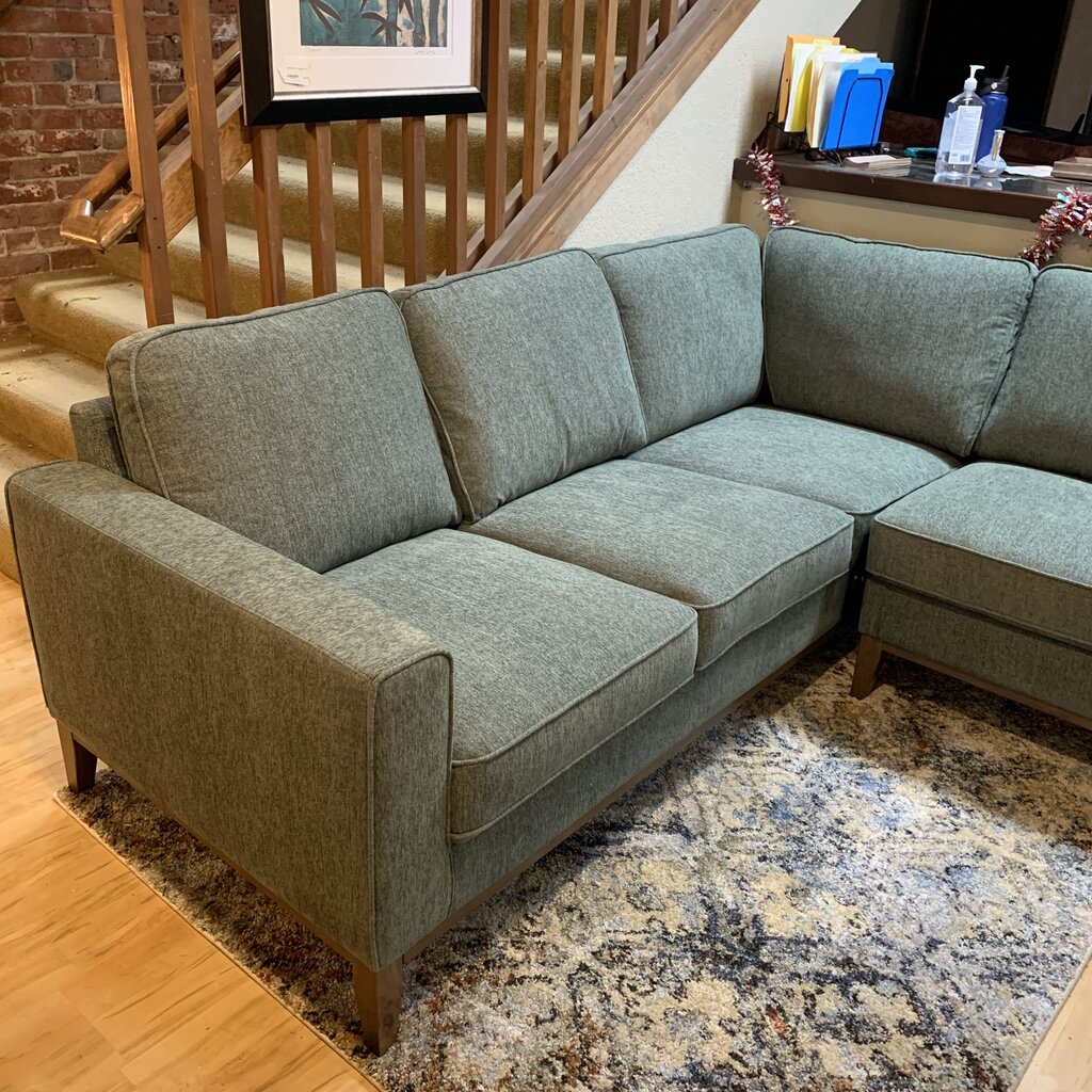 Gray sectional sofa in a living room setting with a staircase and decor items in the background.