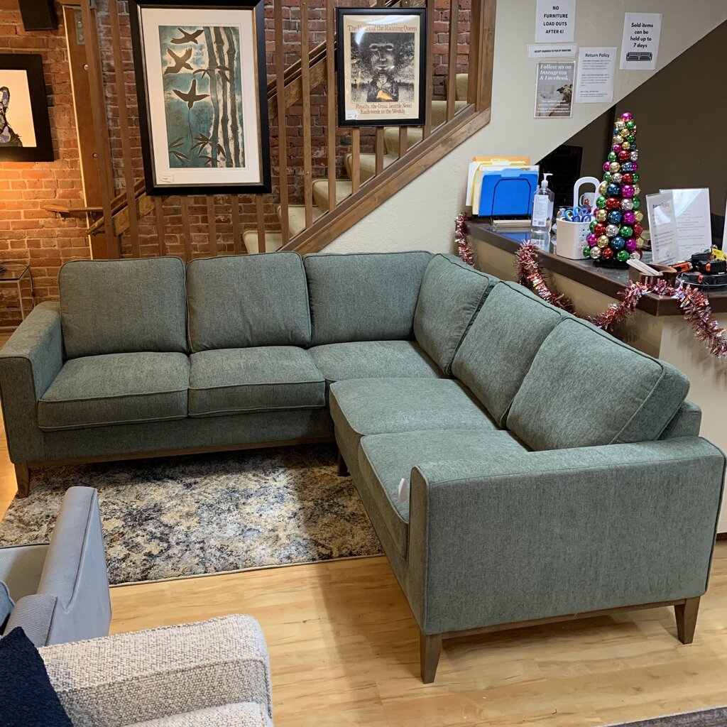 Gray sectional sofa in a room with a brick wall, staircase, and Christmas decorations.