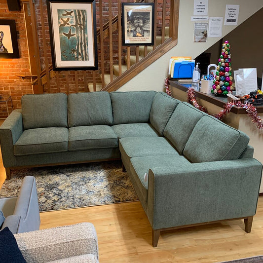 Gray sectional sofa in a room with a brick wall, staircase, and Christmas decorations.