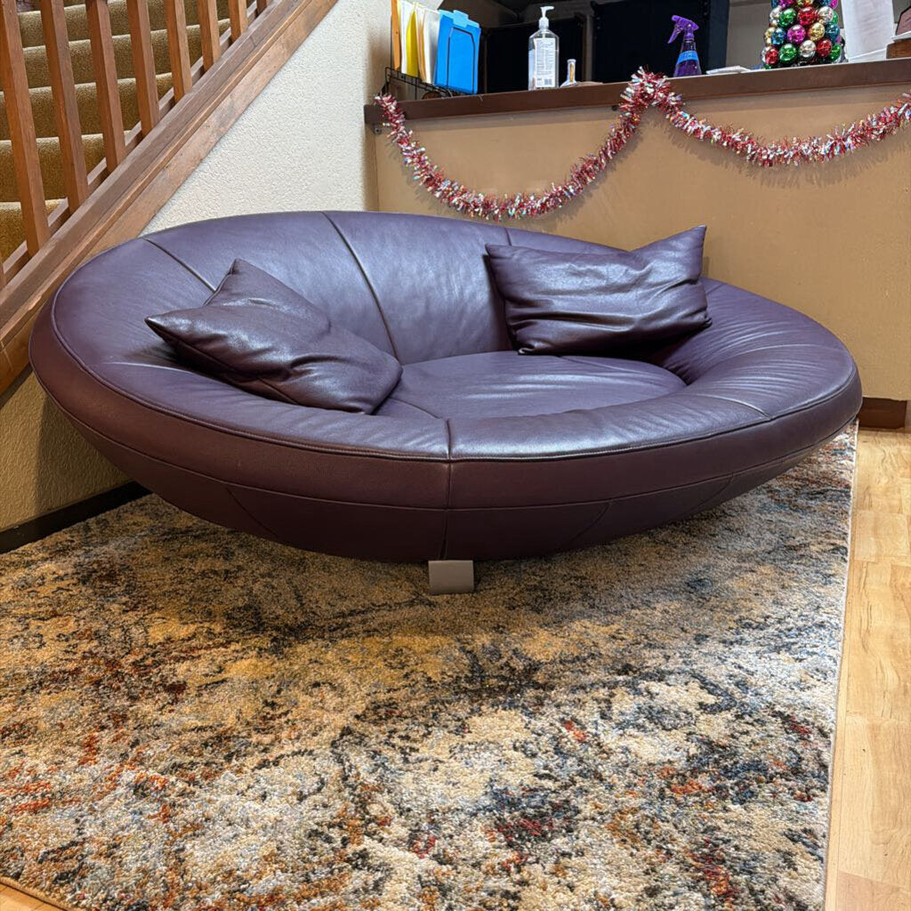 Round leather sofa on a marble floor with a staircase and decorative items in the background